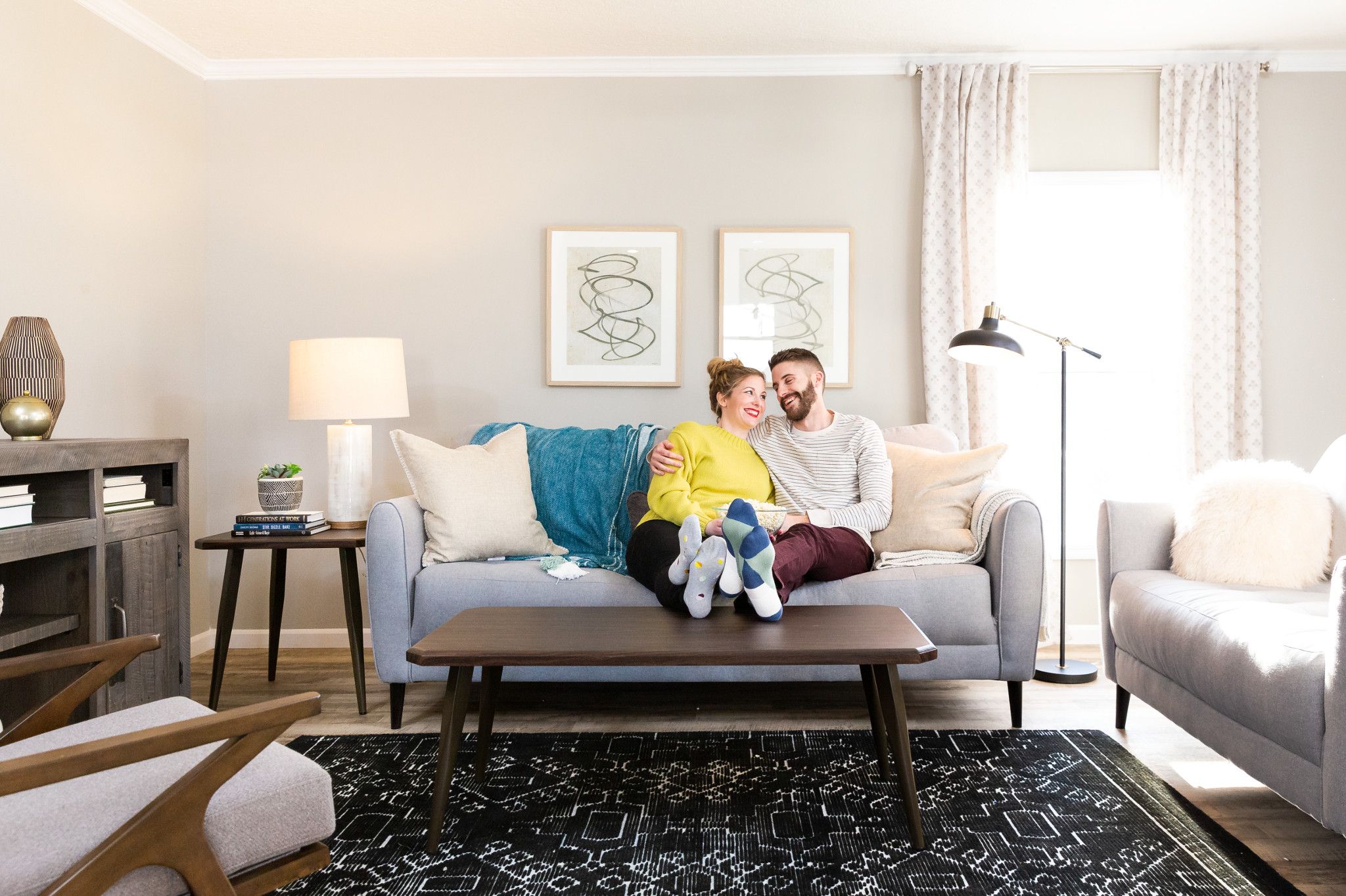 A couple sits on the couch in the living room of their modular home. The living room is decorated with paintings and white furniture, as well as an area rug. Mobile homes for sale near you can also be comfortable and stylish like this.