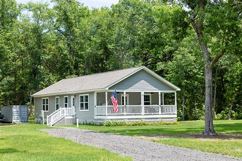 The exterior of a modular home with a wide front porch surrounded by trees.
