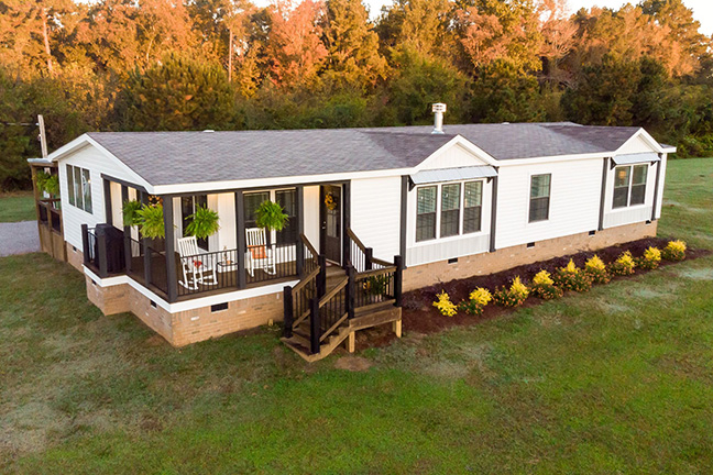 A well-maintained, white manufactured home with an L-shaped porch