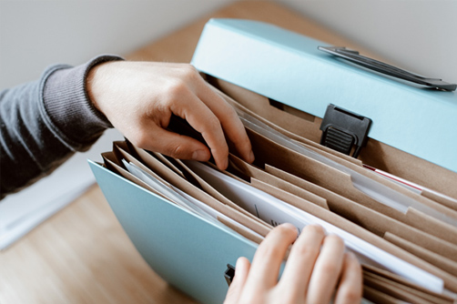 Person selecting papers from an accordion folder in preparation for their Homeowner Assistance Fund application.